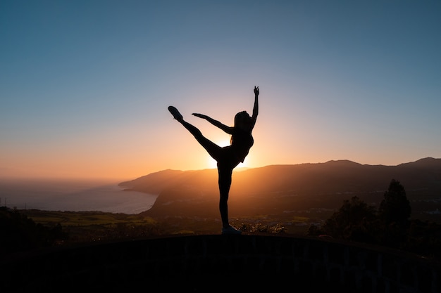 Silhouette of woman enjoying freedom feeling happy at sunset with mountains and sea