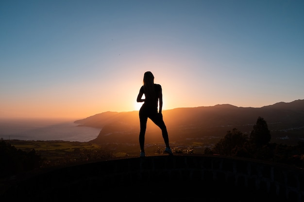 Silhouette di donna che gode della libertà sentirsi felice al tramonto con le montagne e il mare