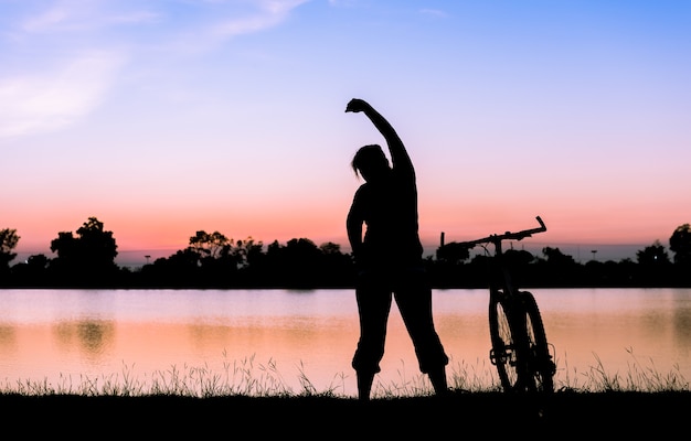 Photo silhouette woman exercise near bicycle on sunset.