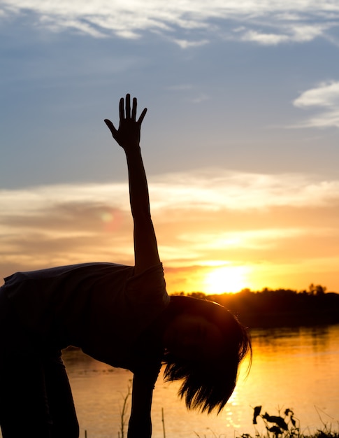 Silhouette of woman exercising over beautiful sunset background.