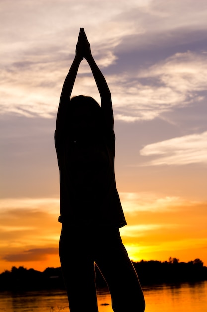 Silhouette of woman exercising over beautiful sunset background.