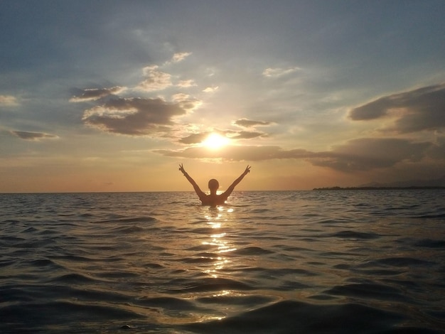 夕暮れの海で平和のサインを示す女性のシルエット