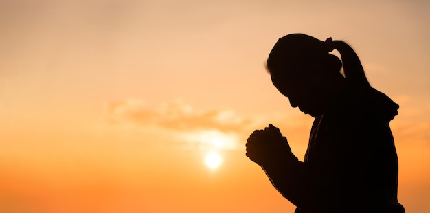 Silhouette of woman hand praying spirituality and religion female worship to god banner with copy space Religious people are humble to God Christians have hope faith and faith in god