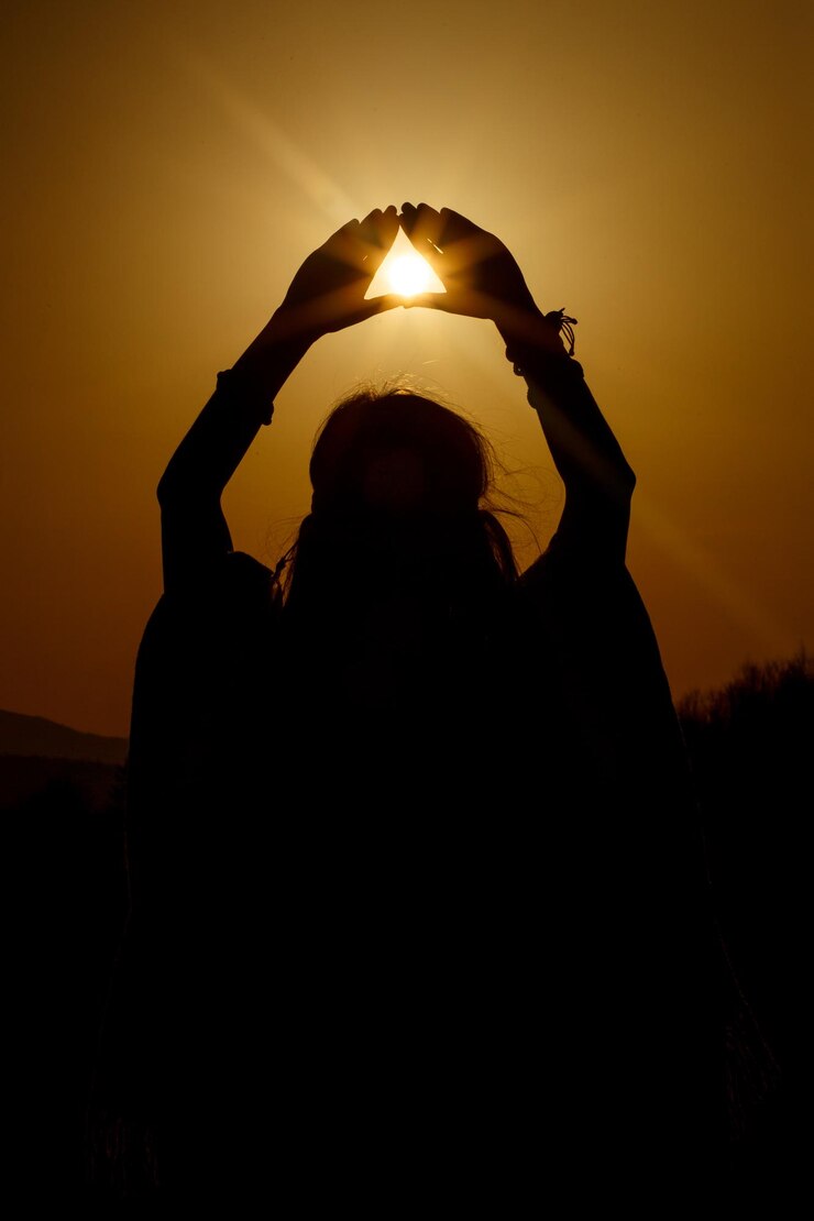 Photo silhouette of woman hands holding sun in triangle on background of beautiful sunset