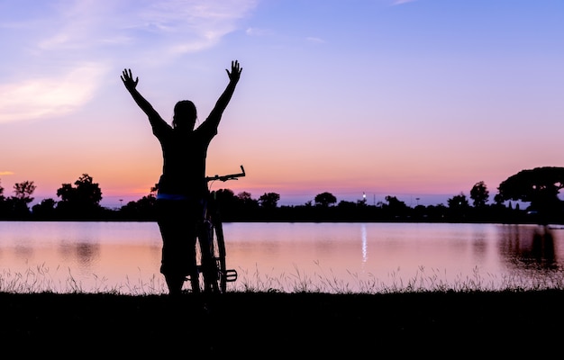 silhouette woman hands up with bicycle on sunset background