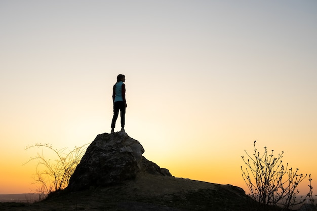 Silhouette di una donna escursionista in piedi da solo sulla grande pietra al tramonto in montagna.