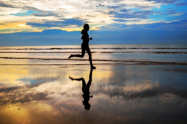 Silhouette of woman jogger running on sunset beach, fitness and healthy life concept