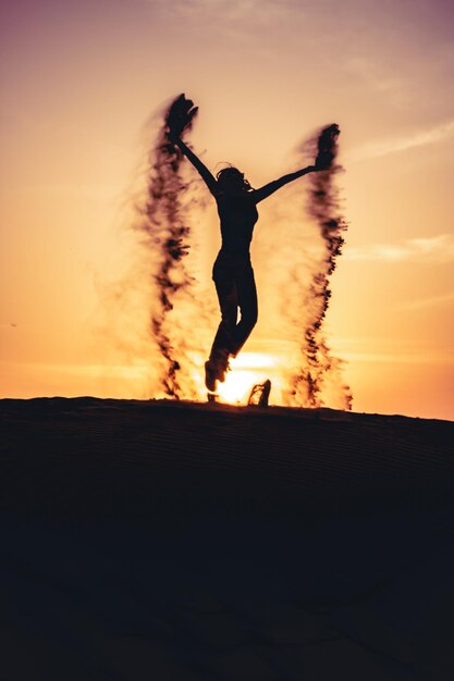 Силуэт женщины, прыгающей на небо во время захода солнца
