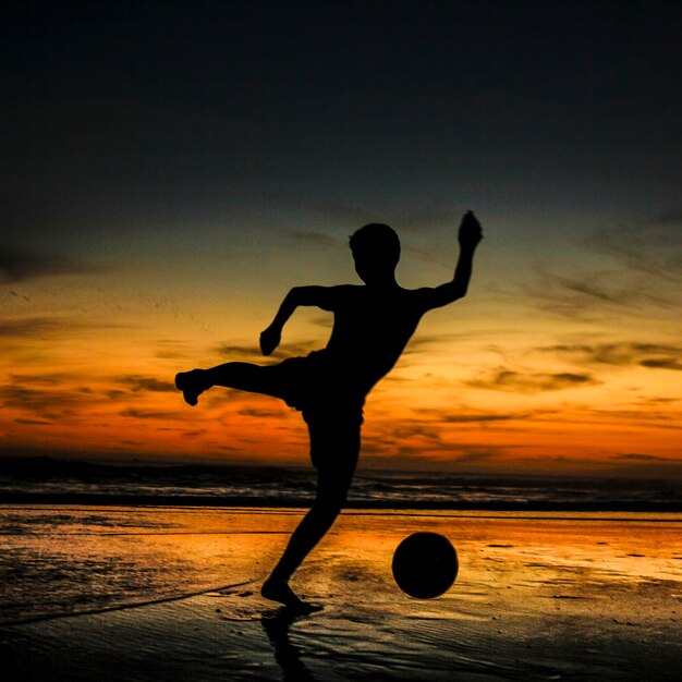 Foto donna a silhouette che salta sulla spiaggia contro il cielo durante il tramonto