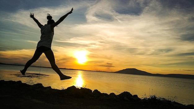 写真 夕暮れの空に向かって海からジャンプする女性のシルエット