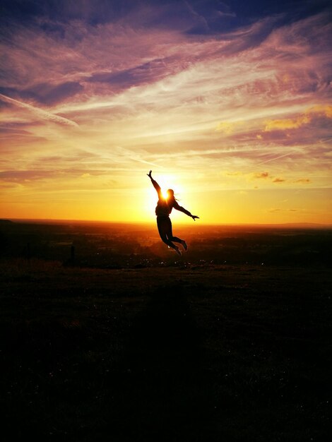 Silhouette woman jumping over field against sky during sunset