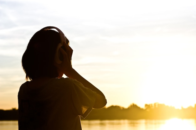 美しい夕日の背景に女性のリスニングの曲のシルエット。