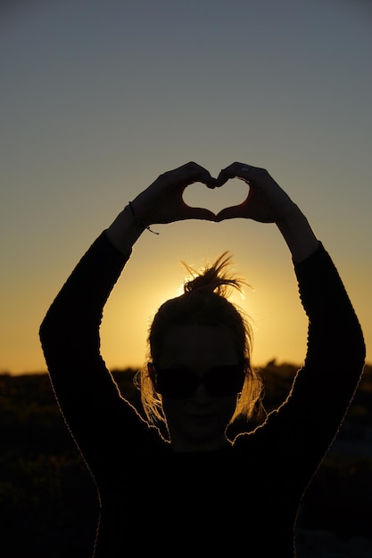 Foto silhouette donna che fa forma di cuore contro il cielo limpido al tramonto