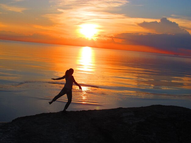 写真 夕暮れの空に照らされたビーチの女性のシルエット