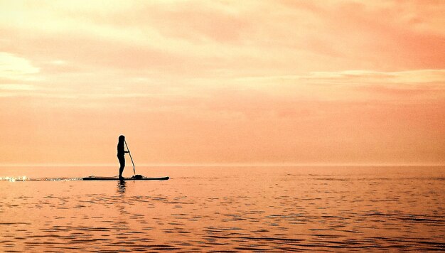 Silhouette woman paddleboarding on sea during sunset