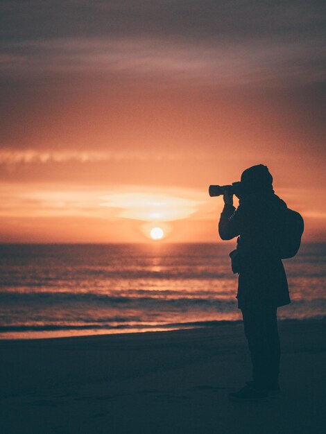 Photo silhouette woman photographing sea against sky during sunset