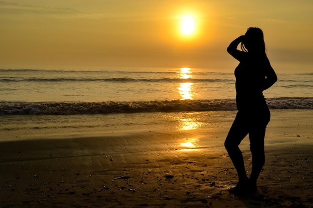 Silhouette of a woman posing sensually on the shore of a beach at sunset The golden hour