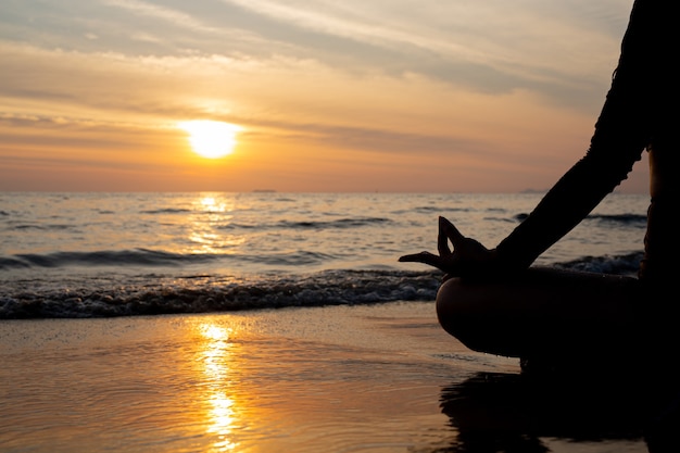 Photo silhouette woman practicing yoga on the beach at sunset.