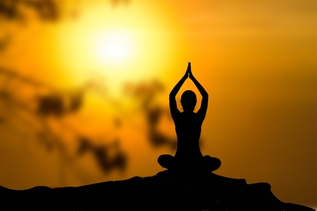 Silhouette of woman practicing yoga at sunset