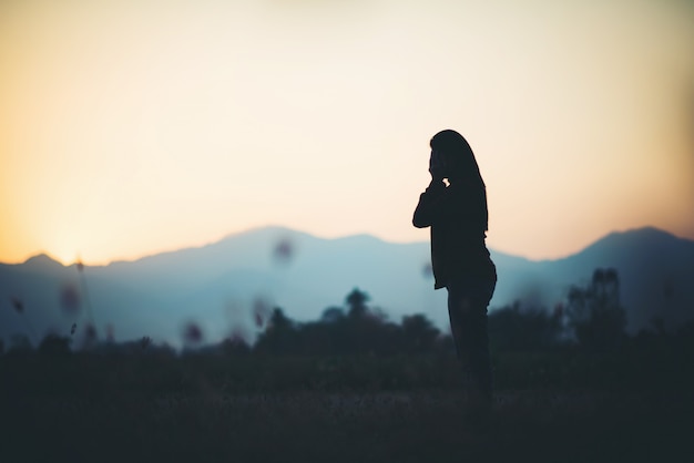 Silhouette of woman praying over beautiful sky background