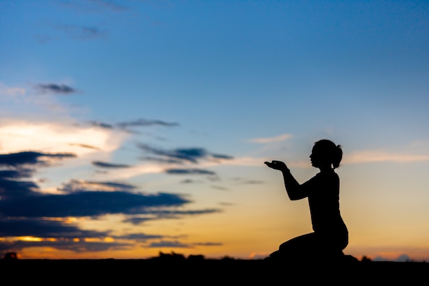 Silhouette donna che prega su sfondo bellissimo cielo