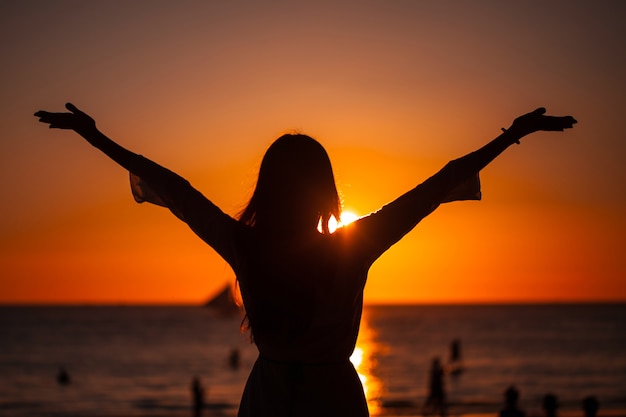 Siluetta della donna che alza le braccia al tramonto dorato sul mare. concetto di libertà, successo e speranza