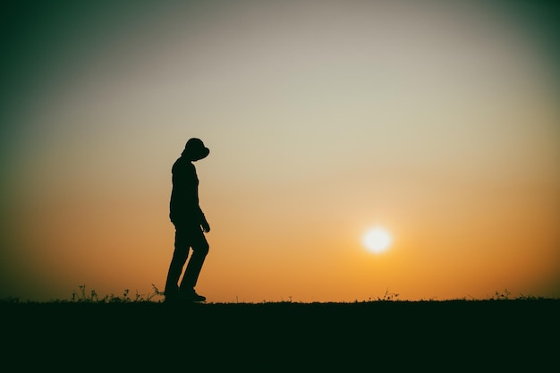 Siluetta della donna triste che cammina lungo il fiume durante il tramonto