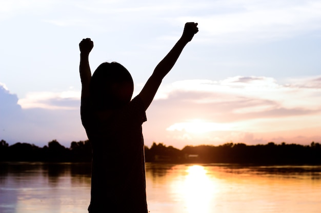 Foto la siluetta della donna mostra le sue mani fa il segno del vincitore sopra il bello fondo stabilito del sole.