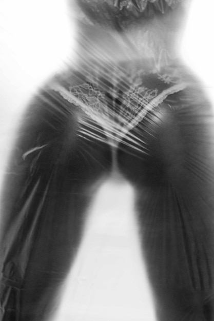 Silhouette woman showing buttocks while standing behind plastic in dark room