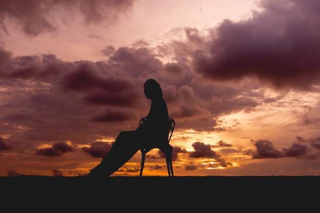 Silhouette of a woman sit on a chair with colorful dramatic sky.