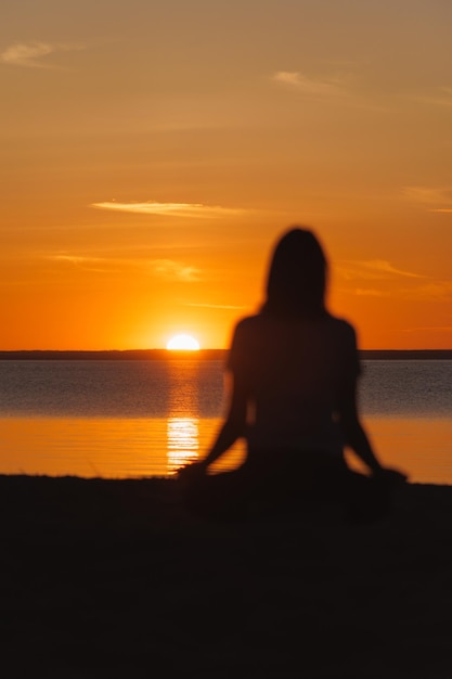 Silhouette woman sitting on beach against sky during sunset