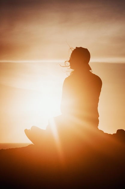 Foto silhouette donna seduta su una roccia contro il cielo durante il tramonto