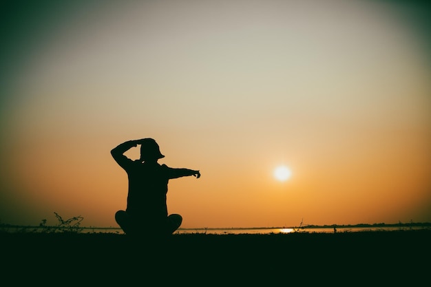 Silhouette della donna seduta triste al fiume durante il tramonto