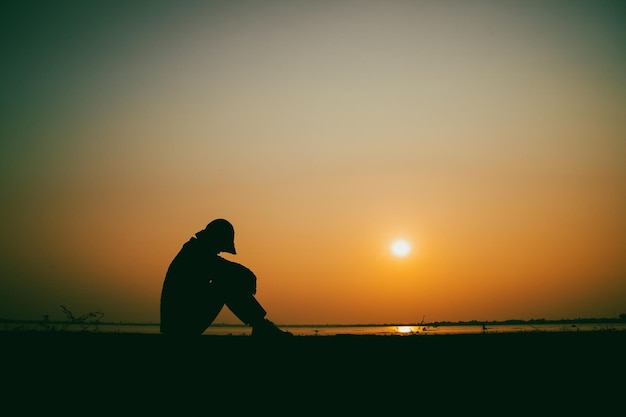 Silhouette of the woman sitting sad at the river during sunset