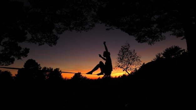 Photo silhouette woman slacklining by trees during sunset