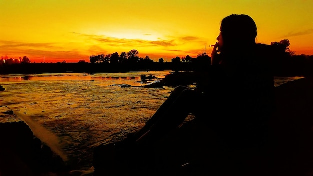 Silhouette woman smoking cigarette at beach against sky during sunset