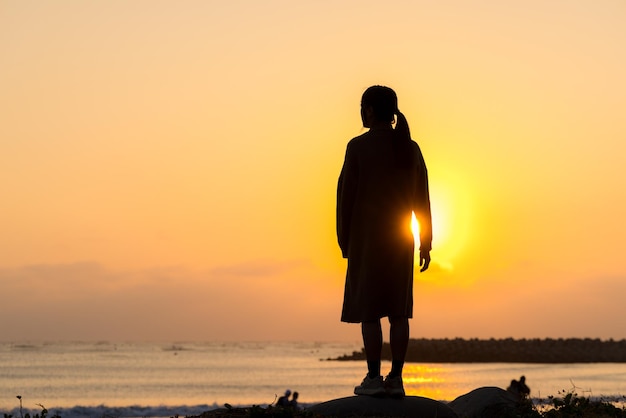 浜辺で日没時に立っている女性のシルエット