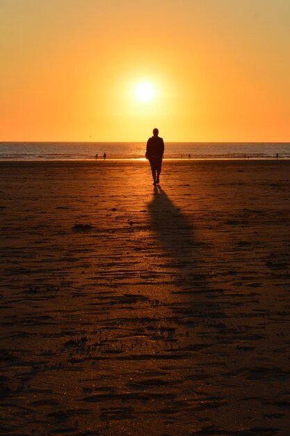 Silhouette woman standing on beach against sky during sunset