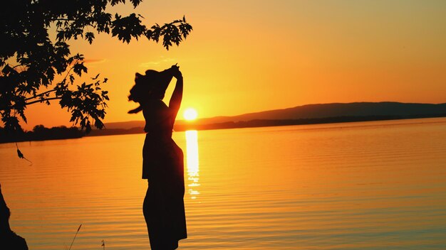 Foto silhouette donna in piedi vicino al lago contro il cielo durante il tramonto