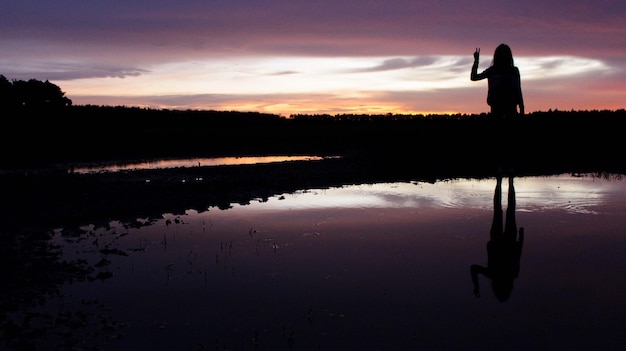 夕暮れの空に照らされた湖のそばに立っている女性のシルエット