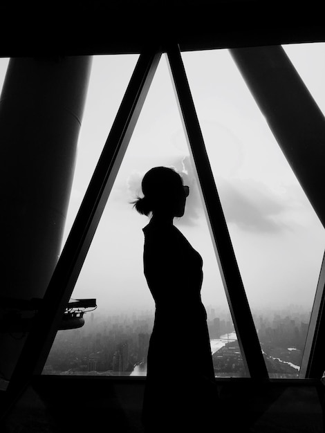 Фото Силуэт женщины, стоящей у окна на фоне неба