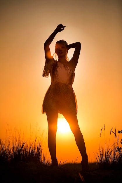 Silhouette woman standing on field against orange sky