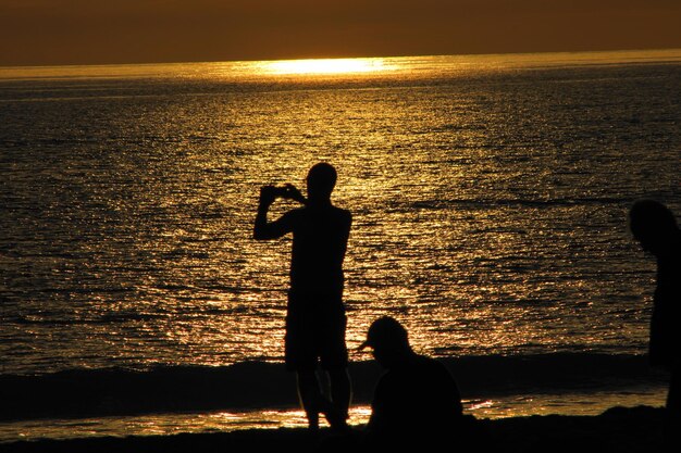 写真 夕暮れの空に照らしてビーチに立っているシルエットの女性