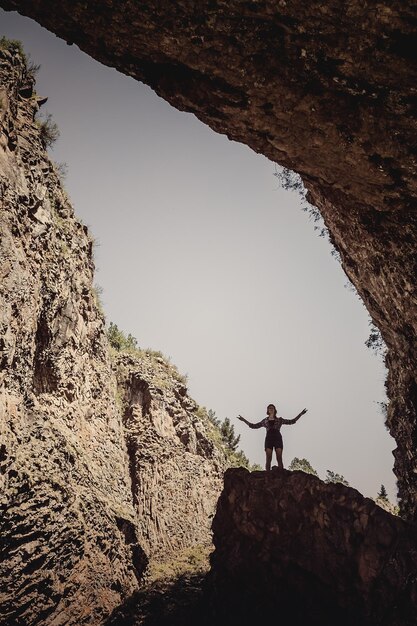 空に対して洞窟の近くの岩の上に立っている女性のシルエット