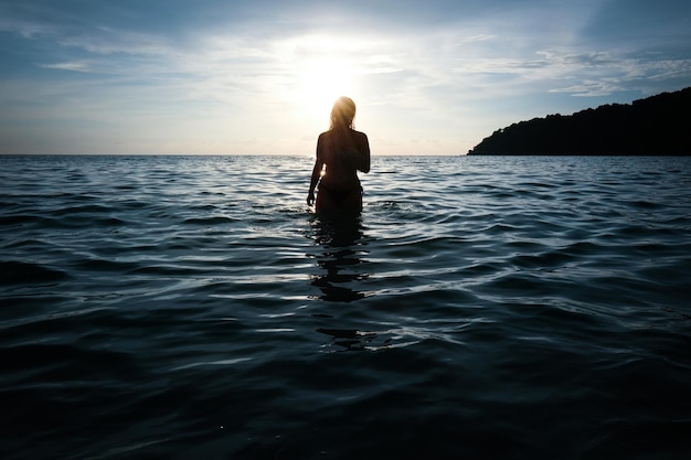 Silhouette woman standing in sea against sky at sunset