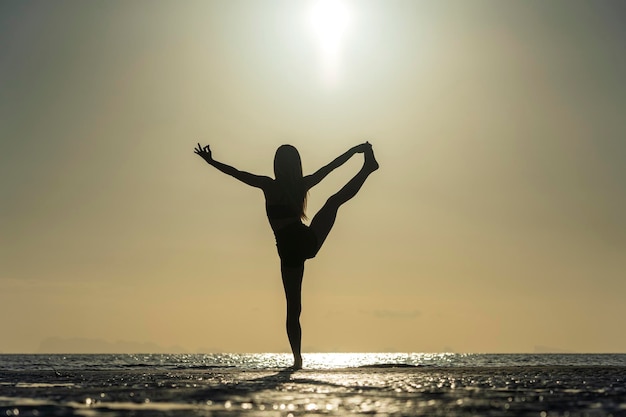 Silhouette of woman standing at yoga pose on the tropical beach during sunset Girl practicing yoga near sea water