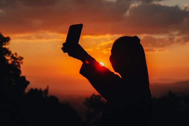 山の美しい夕日の真っ只中に写真を撮る女性のシルエット。