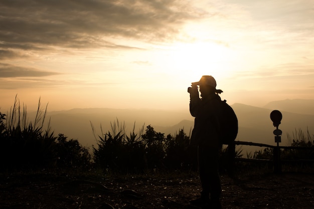 カメラを使用して女性旅行者のシルエットは、美しい夕日の背景に写真を撮る