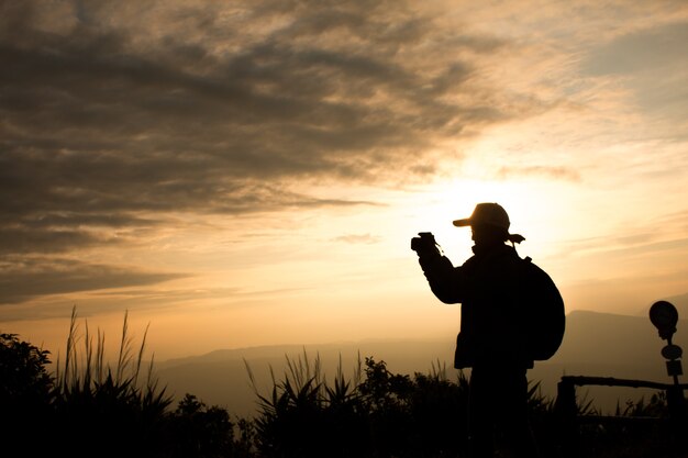 カメラを使用して女性旅行者のシルエットは、美しい夕日の背景に写真を撮る