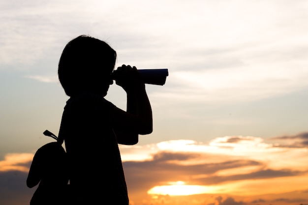 Silhouette of woman use binocular to view long distance subject.